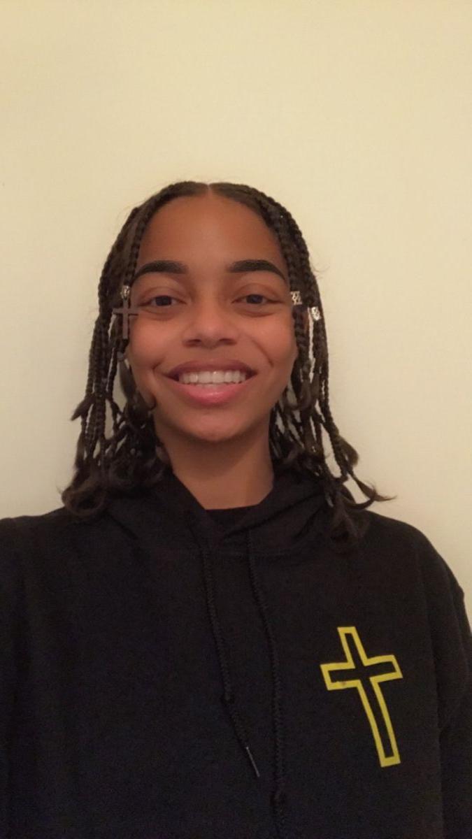 Smiling African American girl; hair in braids with hair jewelry; wearing a black sweatshirt with a picture of a gold cross.